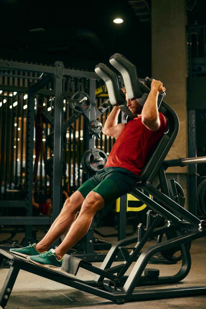 Athletic man doing legs exercise on squat machine at the gym