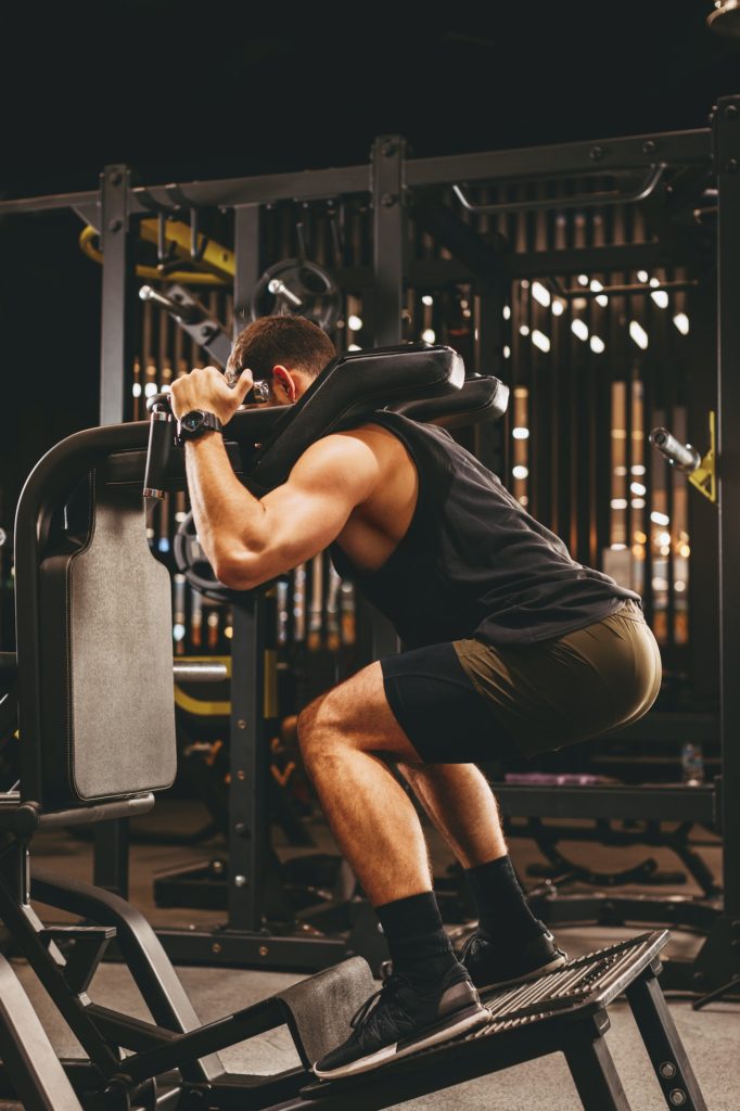 Athletic man doing legs exercise on squat machine at the gym