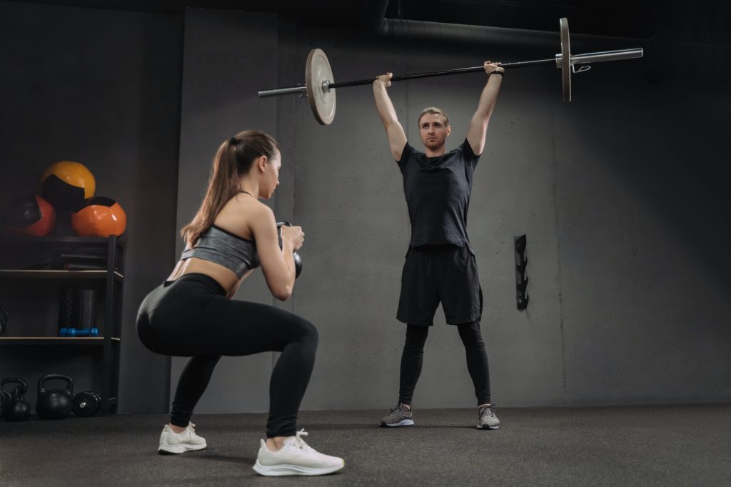 Fit caucasian couple doing crossfit exercises at dark gym