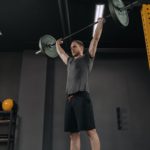 Sportsman holding barbell overhead at dark gym