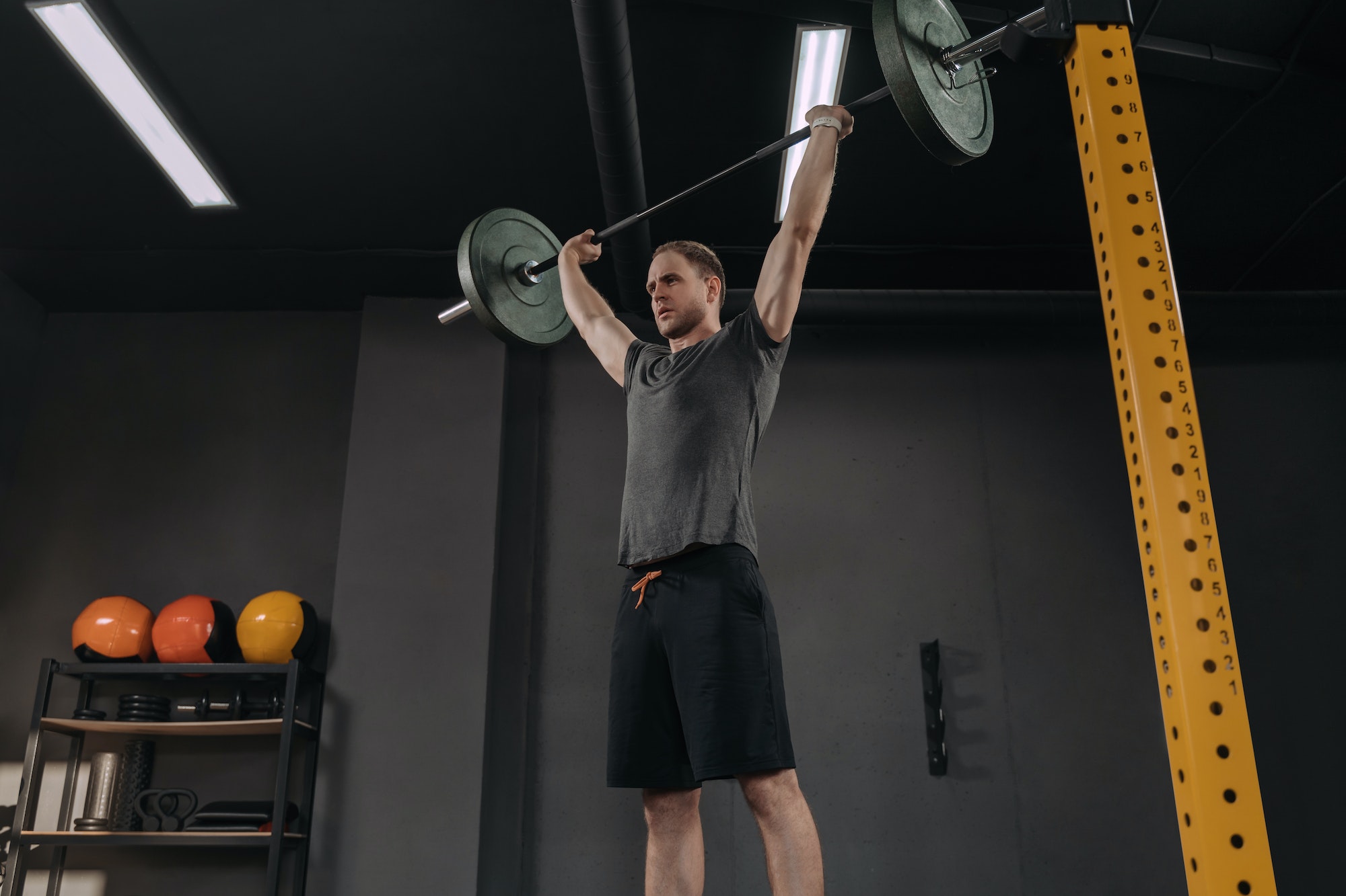 Sportsman holding barbell overhead at dark gym